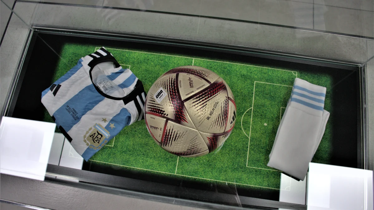Balón de fútbol entre una camiseta argentina y medias blancas dentro de una vitrina