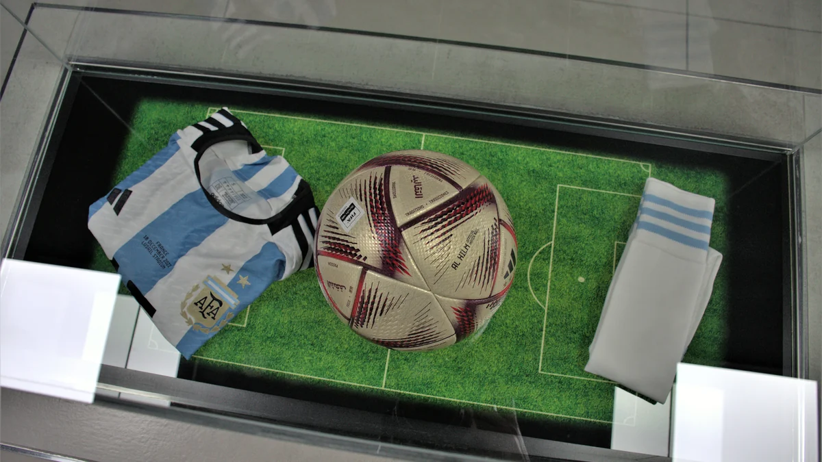 Vista superior de una camiseta de Argentina, un balón y medias en una vitrina con diseño de campo