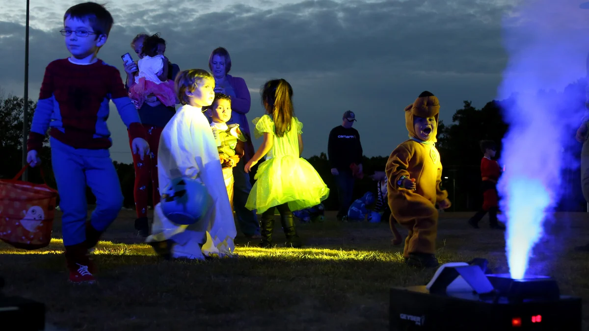 Des enfants costumés marchent de nuit près d’une machine diffusant une fumée bleue éclairée