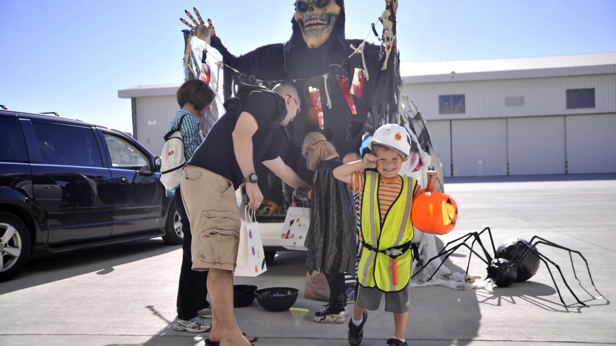Enfant avec un casque blanc, un gilet jaune et un seau citrouille devant des décorations d’Halloween