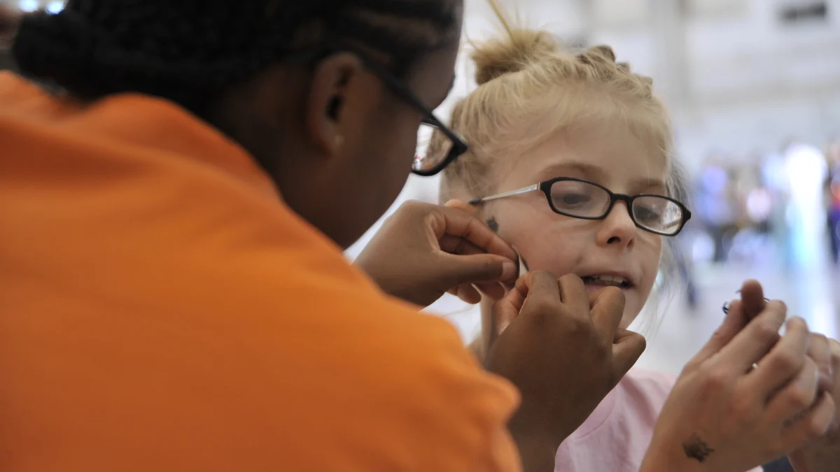 Une personne applique une peinture sombre sur la joue d’une fille portant des lunettes