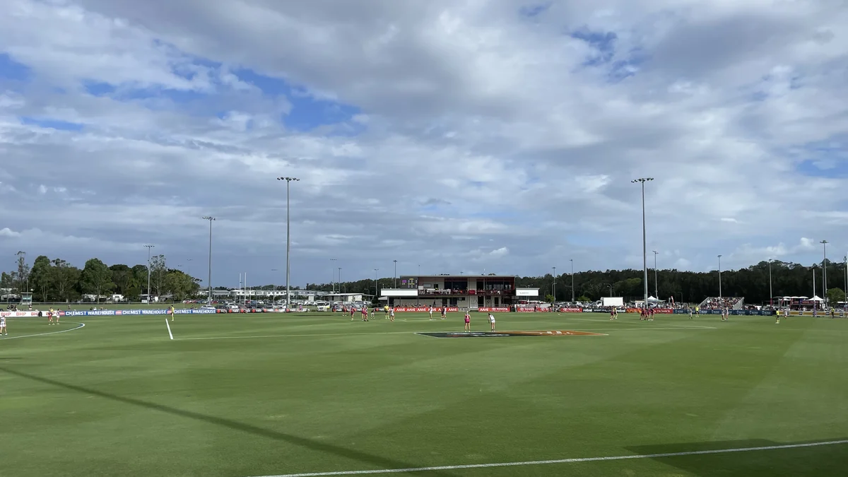Vista amplia de un campo ovalado de fútbol australiano con jugadoras distribuidas por el césped
