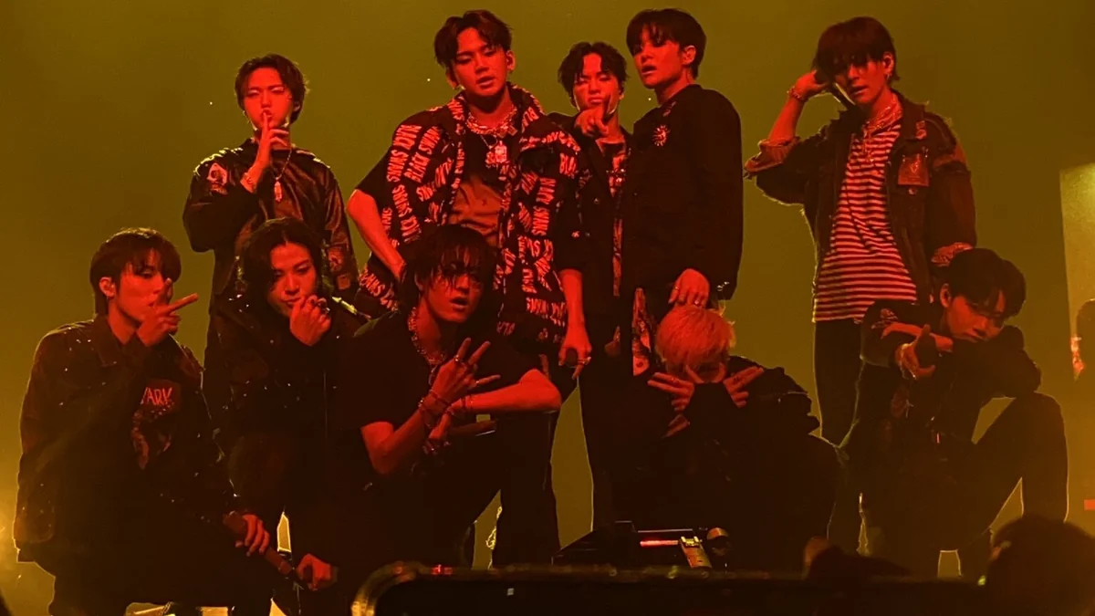 TREASURE members pose together onstage under red and yellow lighting