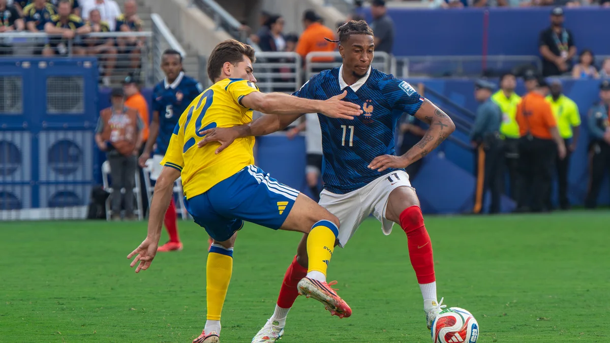 Michael Olise, con la camiseta azul número 11 de Francia, disputa el balón con un jugador de amarillo