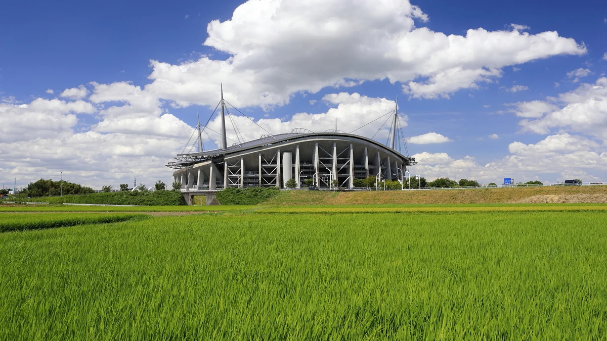 Toyota Stadium seen from a distance behind a green field under a blue, cloudy sky