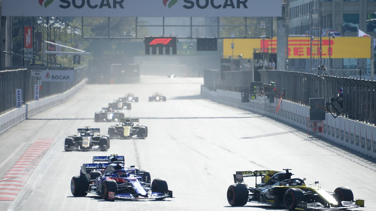 Formula 1 cars battle for position on a long straight bordered by safety barriers.