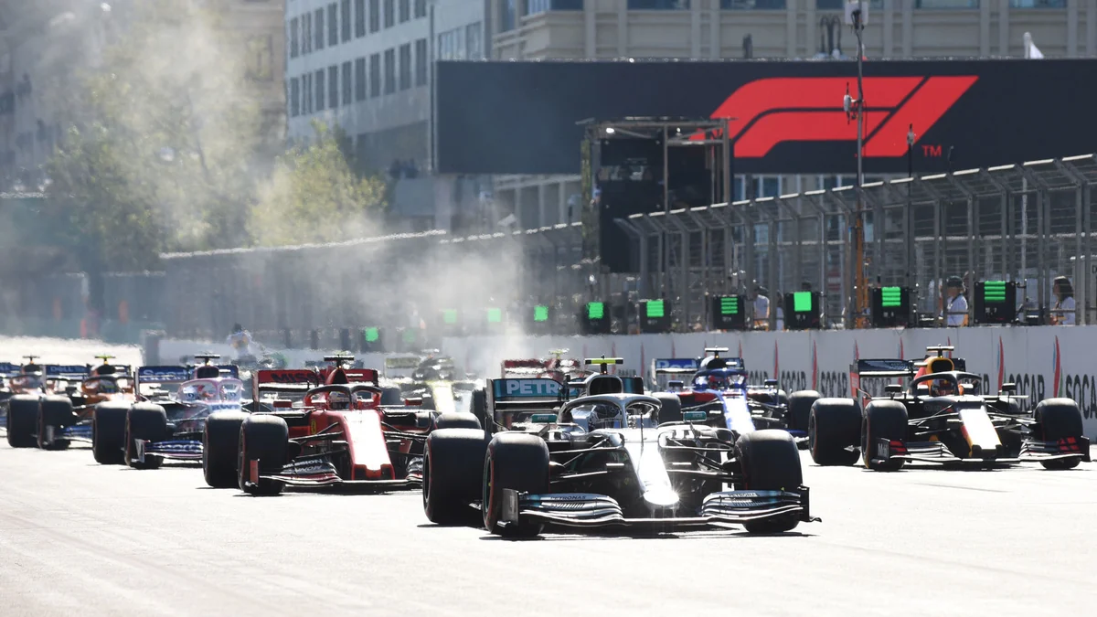 A tightly packed field of Formula 1 cars advances along a straight with an F1 sign in the background.