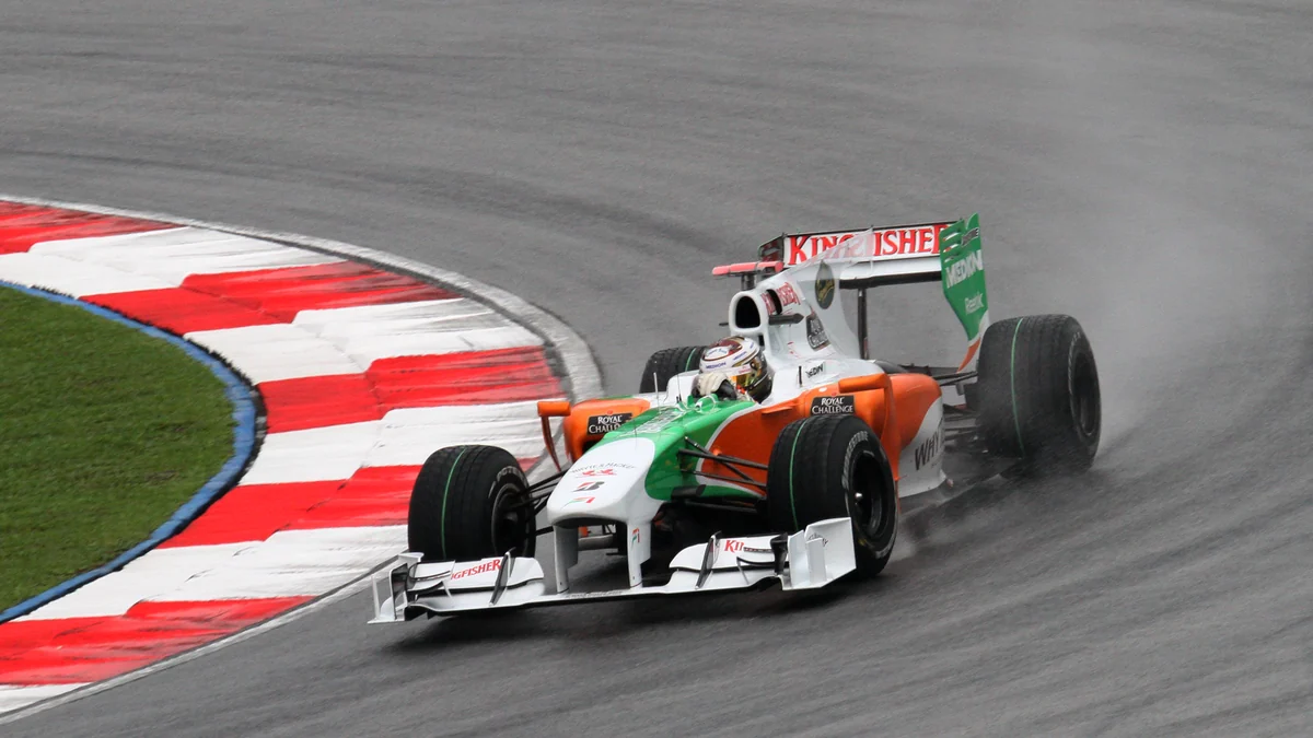 Green, white and orange Formula 1 car taking a wet corner