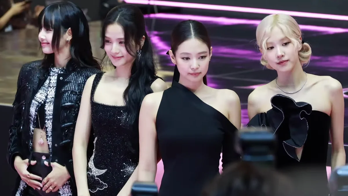 Quatro integrantes do BLACKPINK posam diante de luzes rosas, com equipamentos de câmera em primeiro plano.