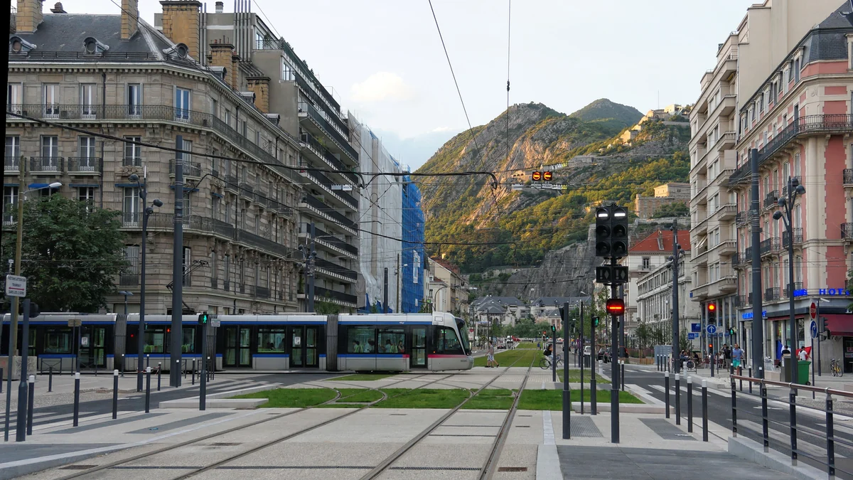 Tram traversant un carrefour urbain devant un versant montagneux