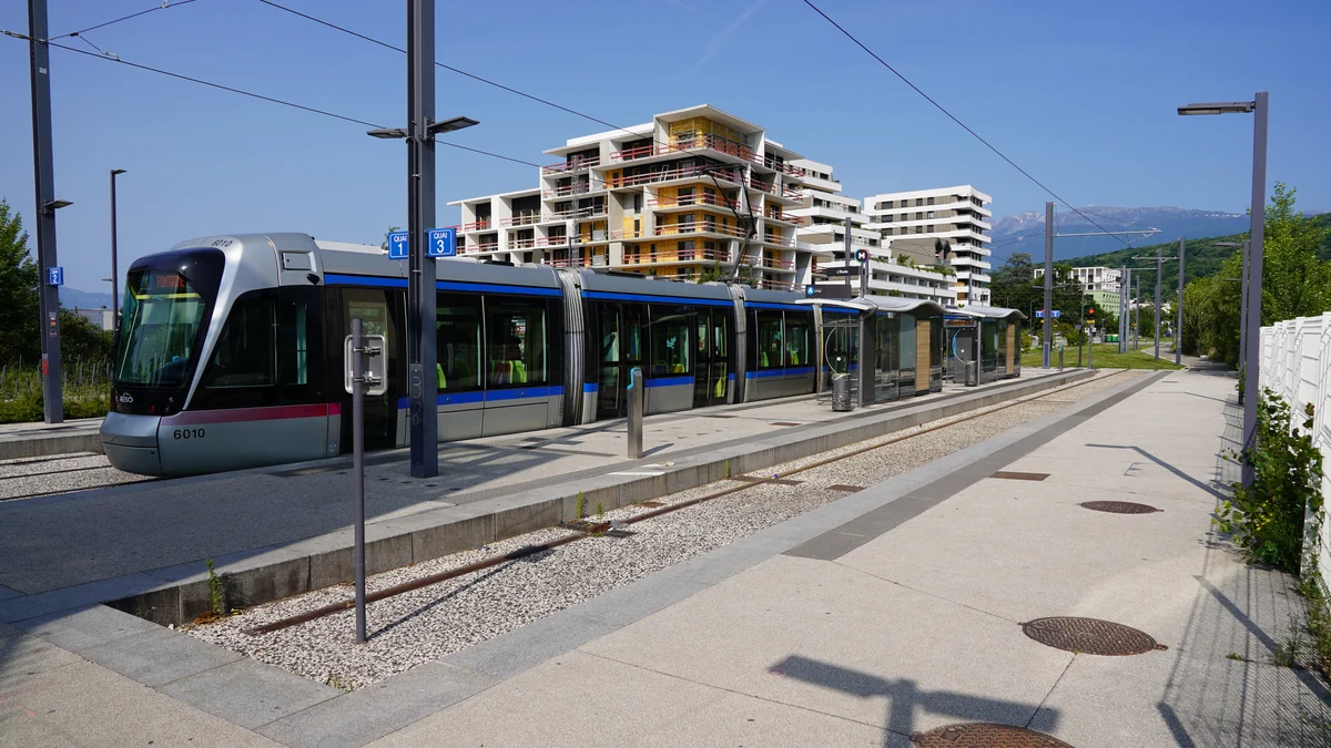 Tram moderne à quai, avec des immeubles et des montagnes à l’arrière-plan