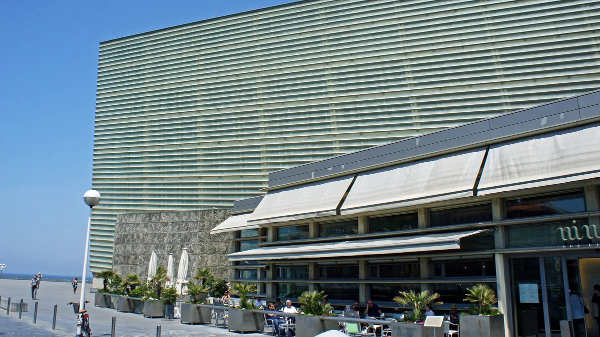 Fachada envidraçada do Kursaal ao lado de um restaurante com mesas externas