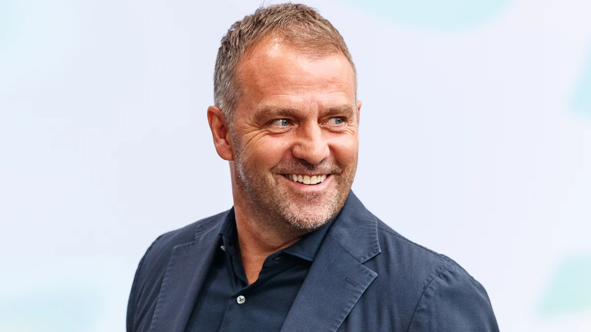 Hansi Flick sourit en regardant sur le côté devant un fond clair