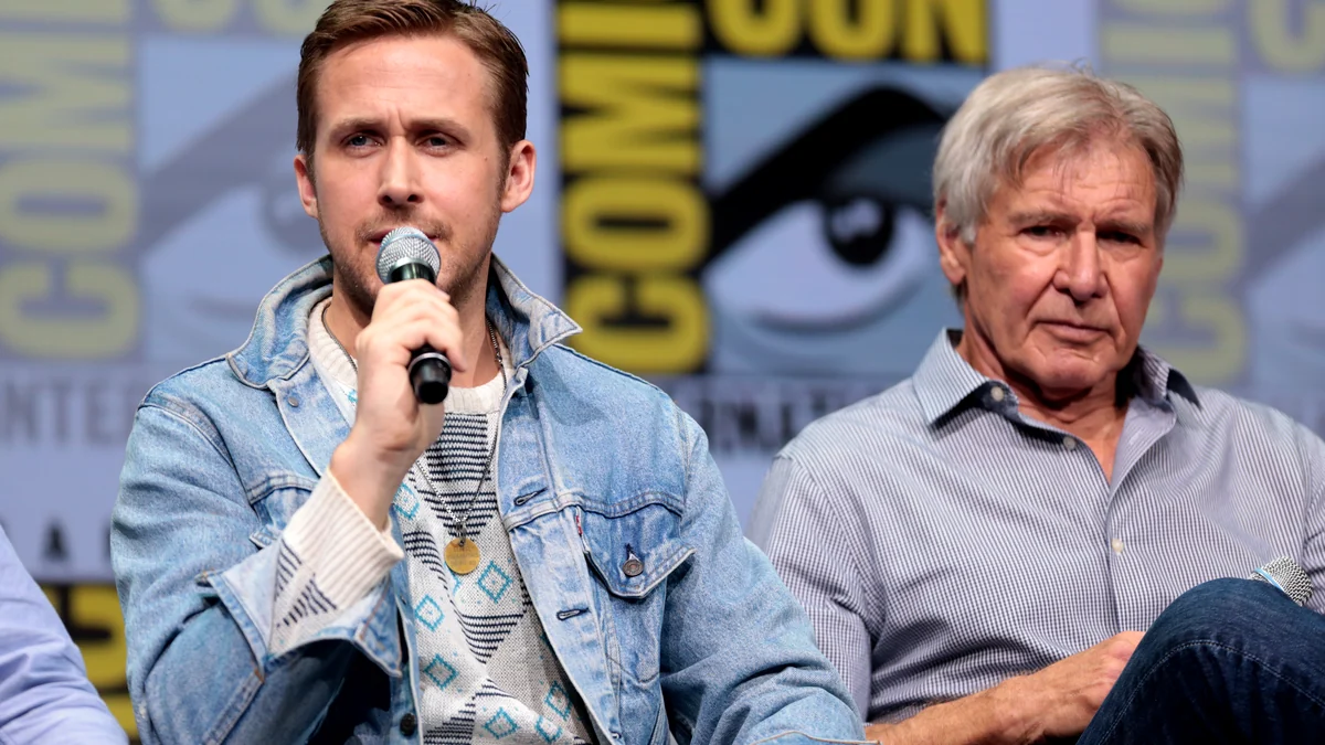 Ryan Gosling habla con un micrófono mientras Harrison Ford está sentado a su lado.