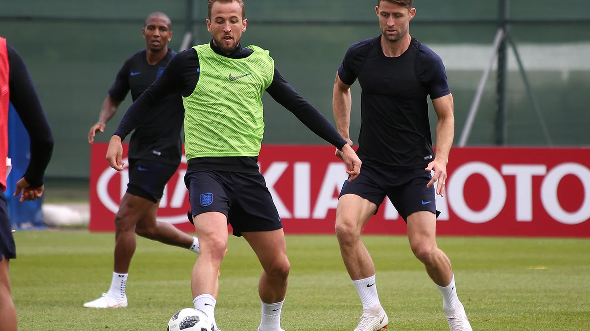 Harry Kane conduz a bola usando colete verde durante um treino da seleção da Inglaterra, acompanhado por outros jogadores.
