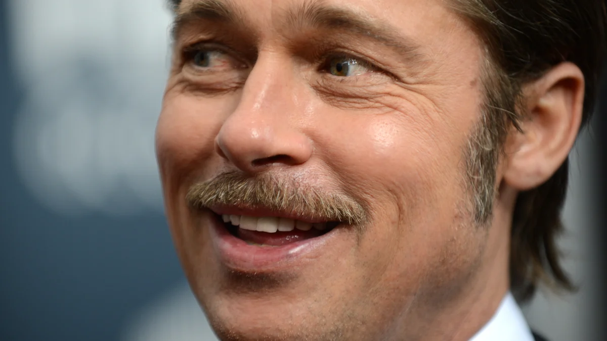 Close do rosto de Brad Pitt sorrindo e usando bigode