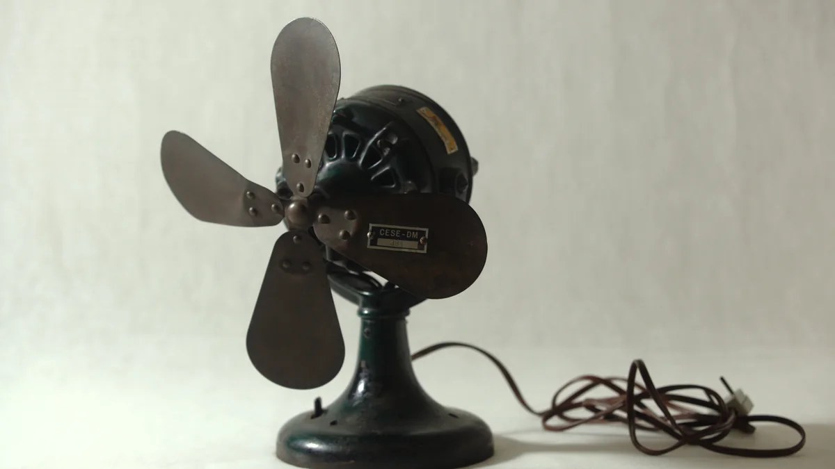 Ventilador de mesa antigo com cinco pás metálicas e fio elétrico sobre uma superfície clara