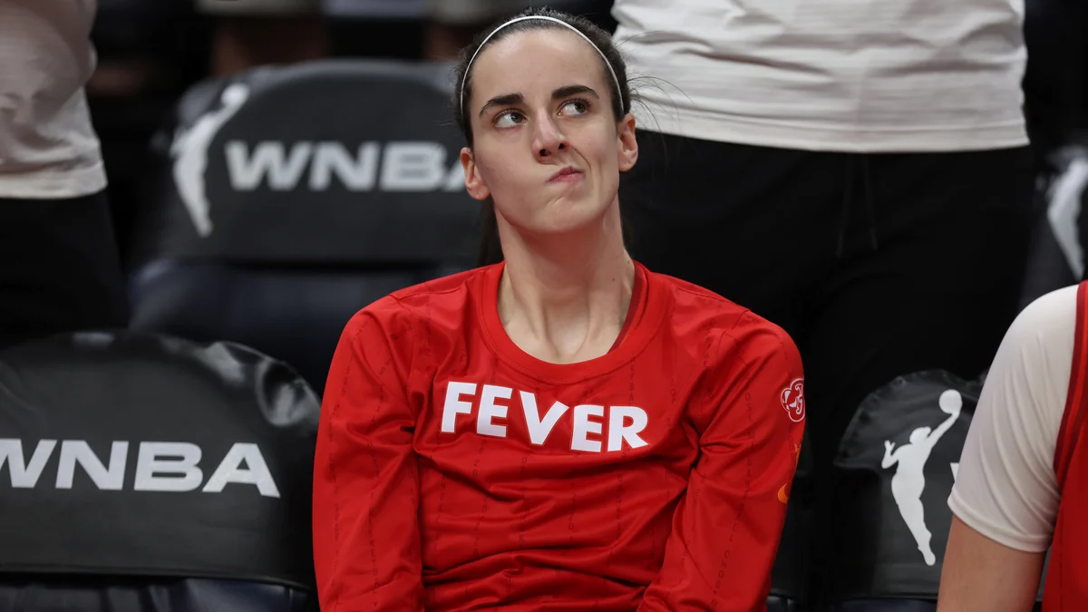 Indiana Fever player seated on the bench in a red shirt with a pensive expression.