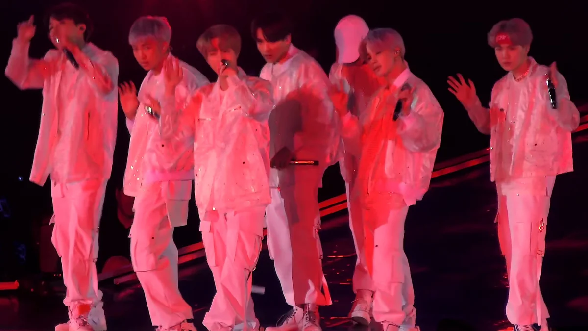 Integrantes de BTS vestidos de blanco bajo iluminación roja en el escenario