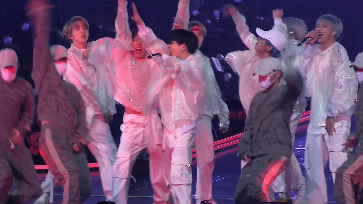 Integrantes de BTS y bailarines actúan en un escenario iluminado