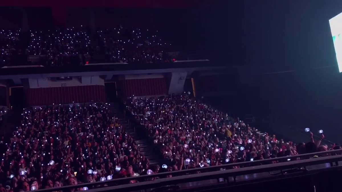 Arquibancadas lotadas com fãs segurando luzes durante um show