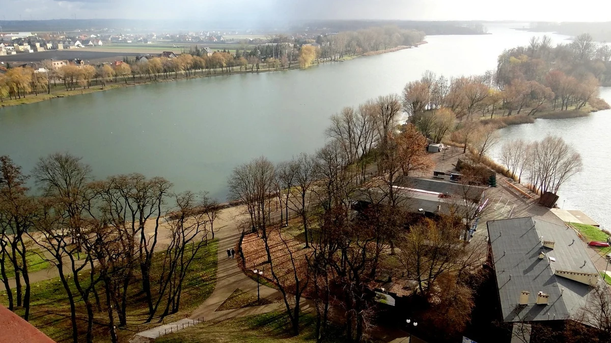Vue en hauteur d’un lac entre des rives boisées, entouré de chemins, de bâtiments et de maisons.