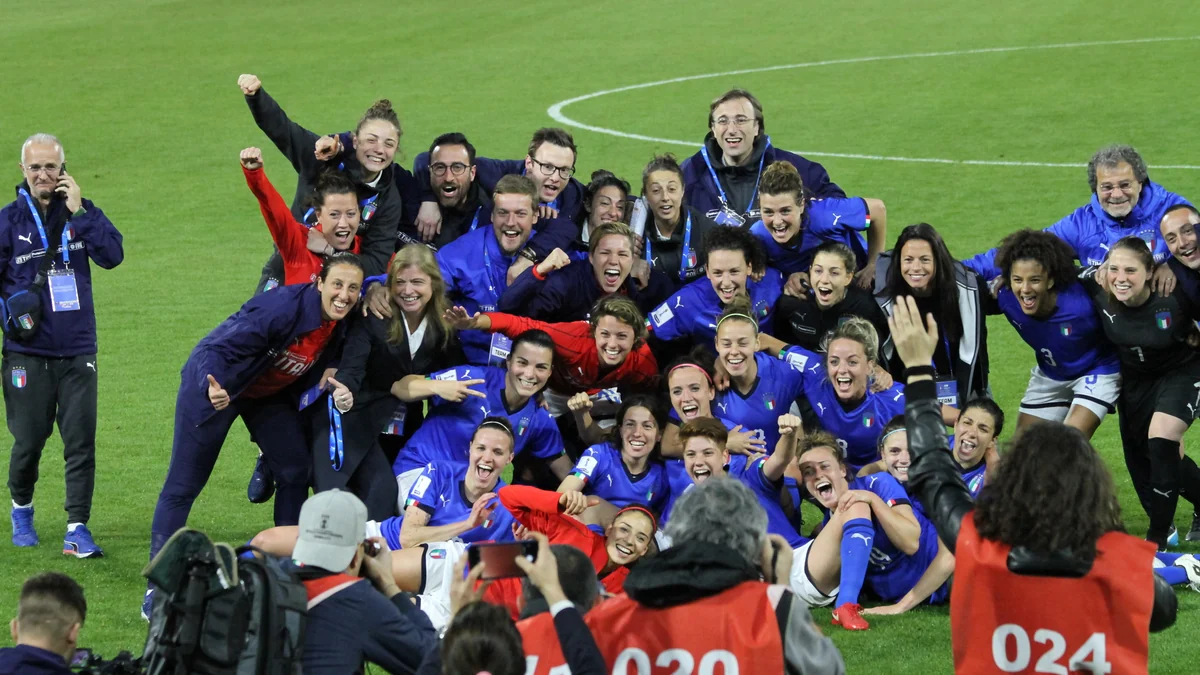 Players and staff from Italy’s women’s football team celebrate on the pitch in front of photographers
