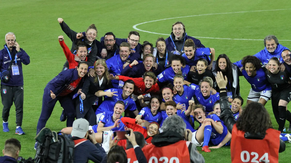 Jogadoras e integrantes da seleção italiana feminina de futebol celebram no gramado diante de fotógrafos