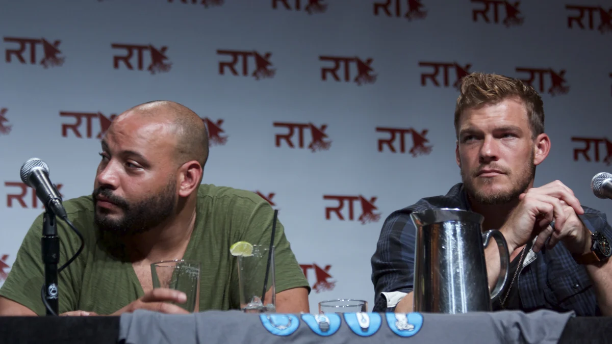 Colton Dunn e Alan Ritchson sentados a uma mesa com microfones durante um painel
