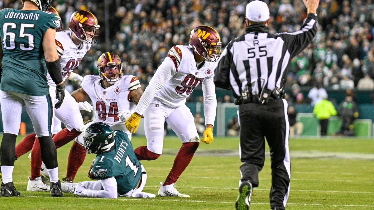 Jalen Hurts sentado no gramado após uma jogada, cercado por jogadores de Washington e um árbitro