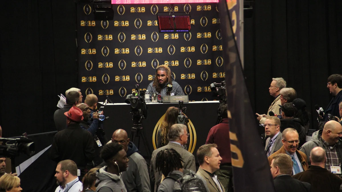 Jalen Hurts sentado diante de microfones em uma entrevista coletiva cercada por jornalistas