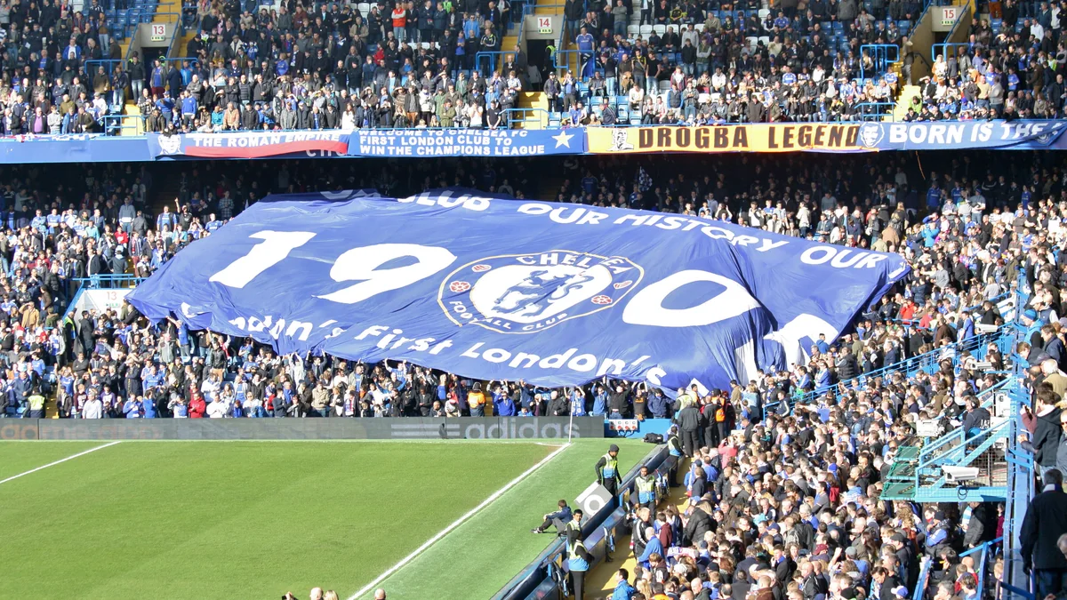 Torcedores do Chelsea seguram uma grande bandeira azul com o escudo e o ano de 1905 nas arquibancadas