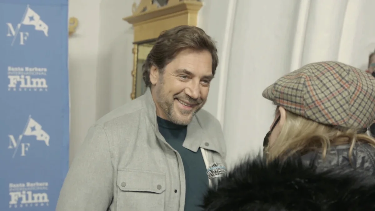 Javier Bardem smiles at an interviewer holding a microphone.