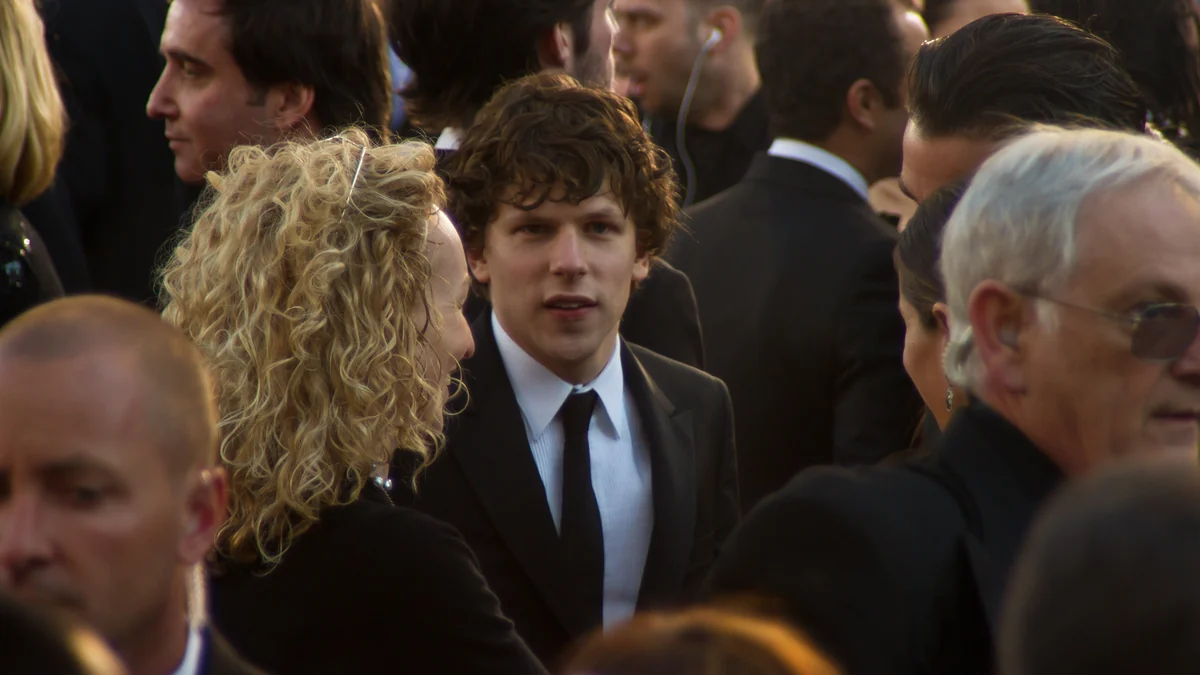 Jesse Eisenberg de terno preto no centro de uma multidão