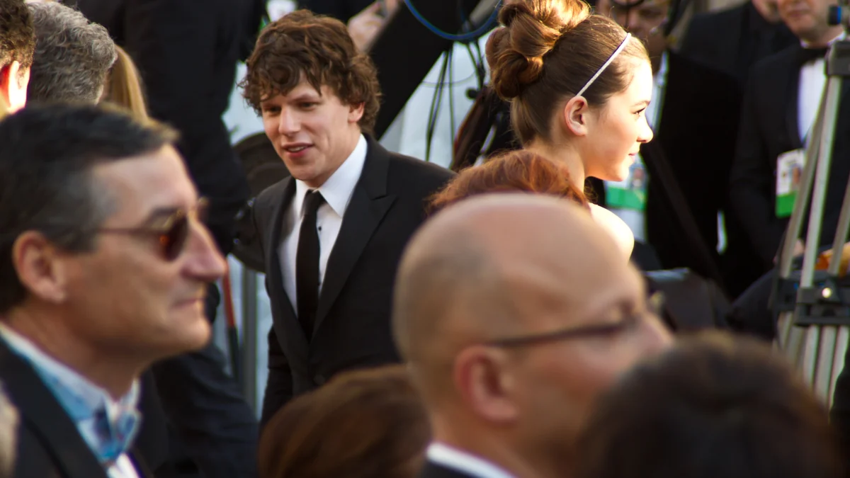 Jesse Eisenberg de terno preto em meio a convidados de um evento
