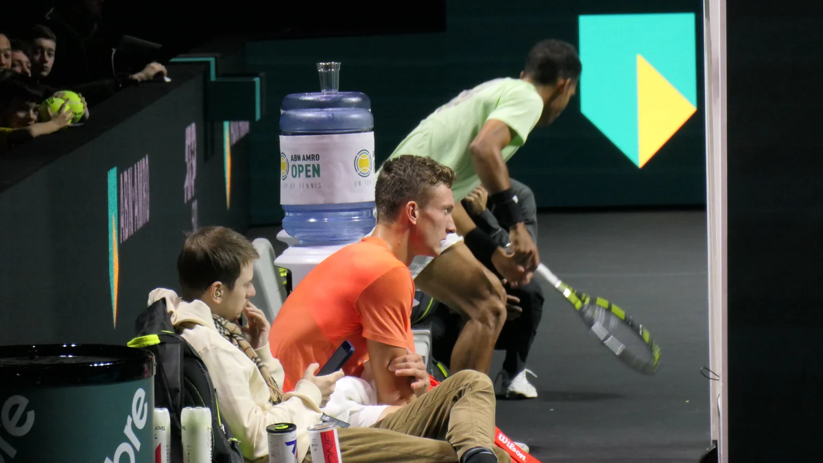 Jiri Lehecka, en maillot orange, assis au bord d’un court de tennis couvert