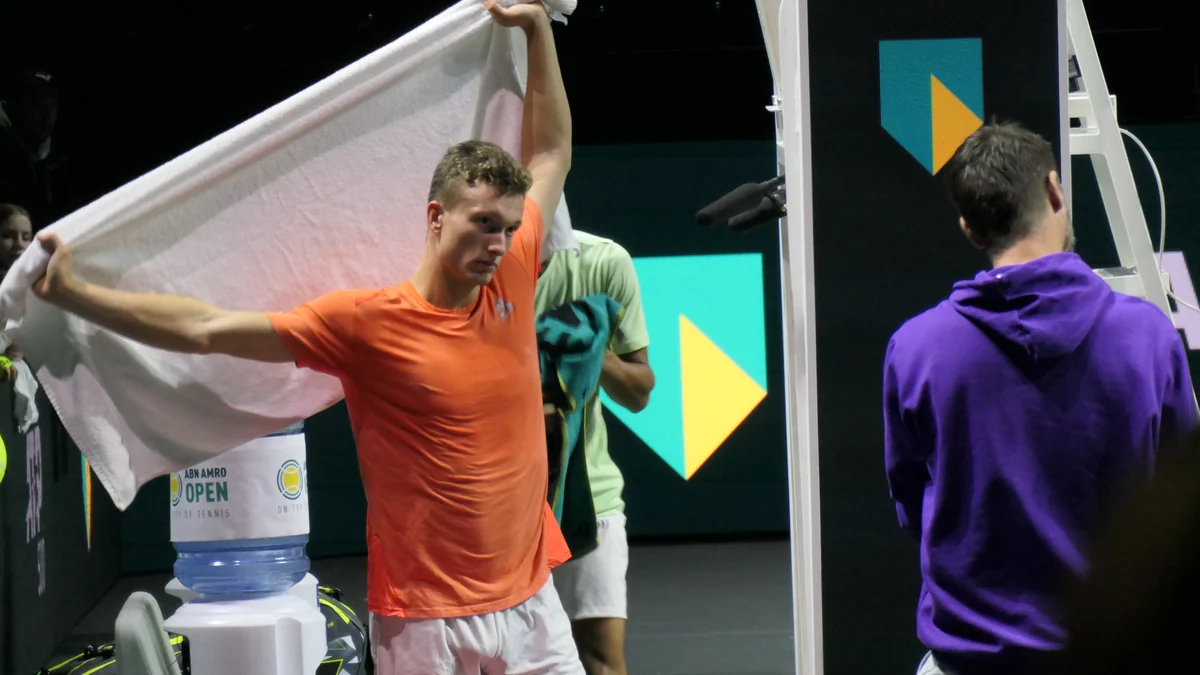 Jiri Lehecka, en maillot orange, lève une serviette blanche au bord du court
