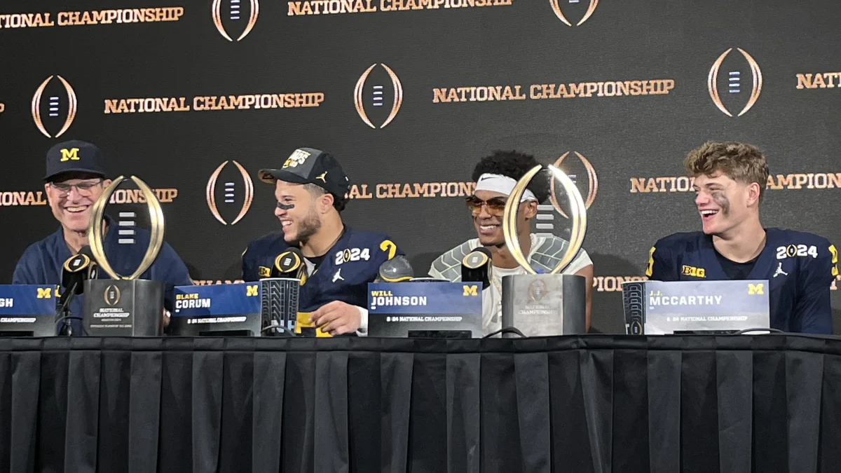 J.J. McCarthy sentado a la derecha de otros integrantes de Michigan en una rueda de prensa, con trofeos sobre la mesa