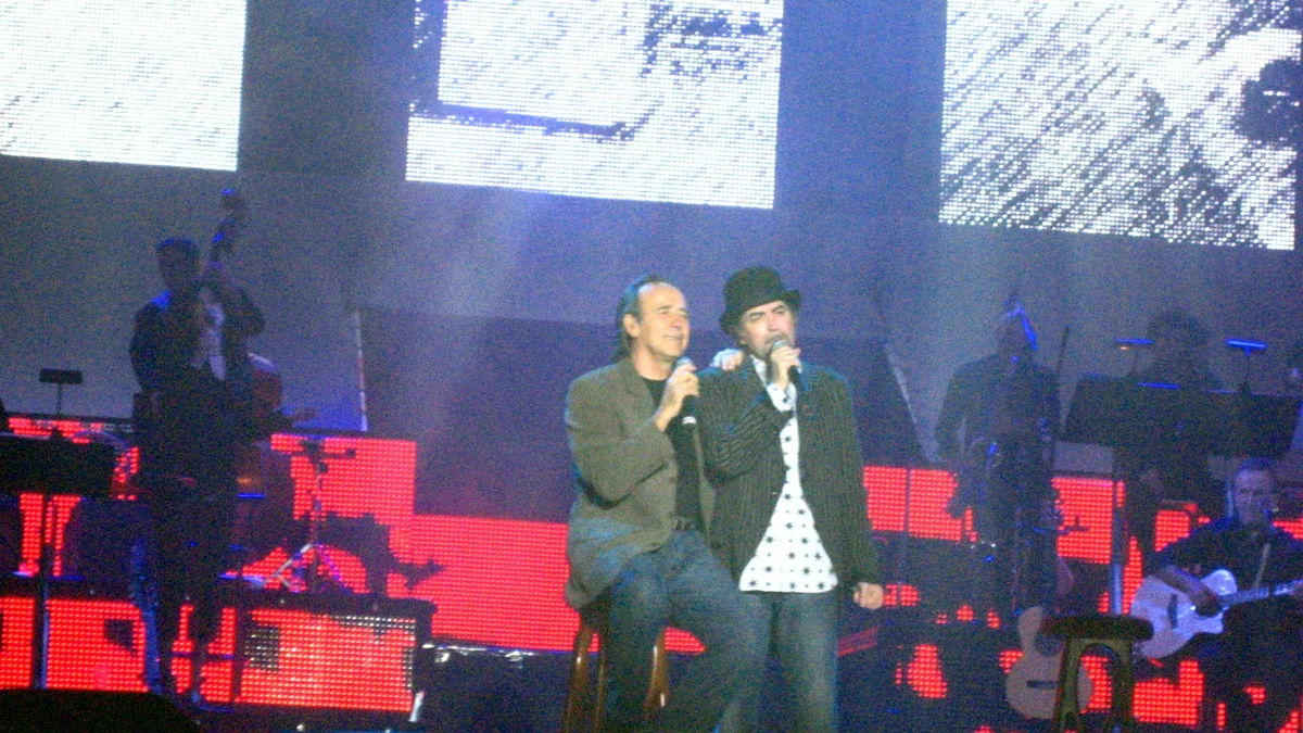 Joan Manuel Serrat and Joaquín Sabina singing together on a lit stage