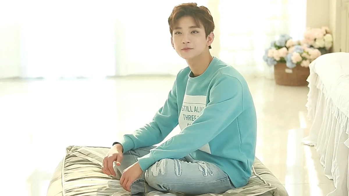 Joshua sits on a cushion wearing a light-blue sweatshirt and jeans in a bright room