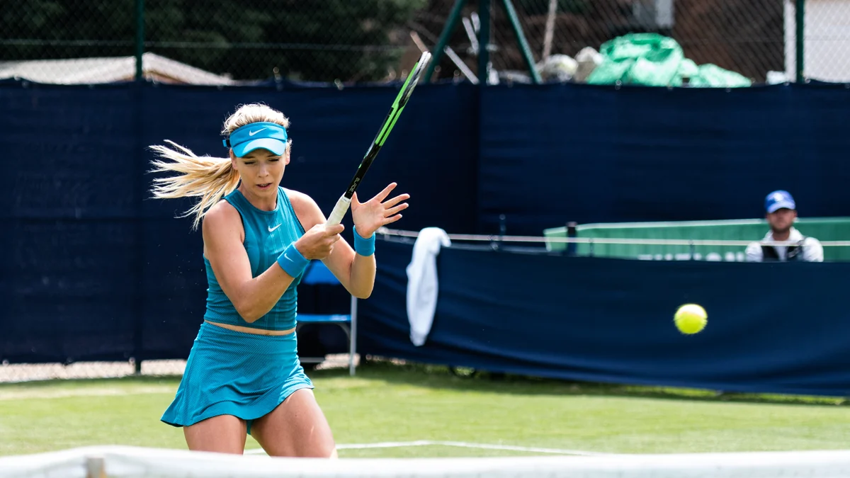 Katie Boulter golpea la pelota en una pista de hierba con la red en primer plano