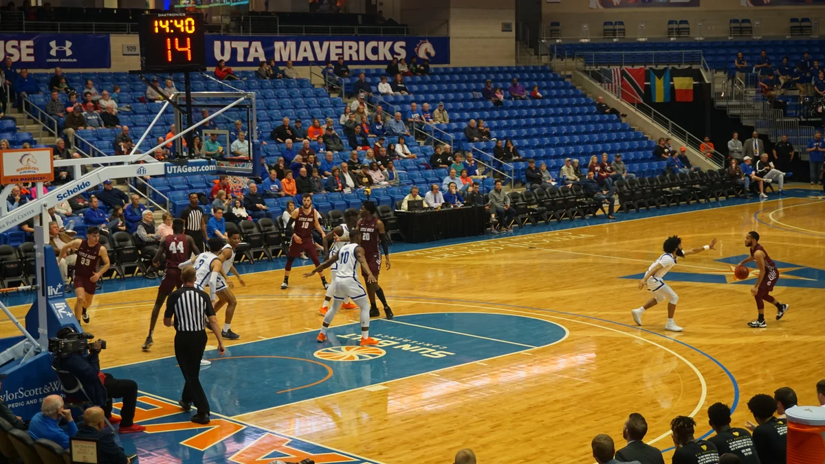Jogador de Little Rock com a bola diante da defesa de UT Arlington em uma quadra coberta
