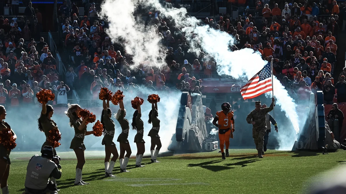 Un joueur des Denver Broncos et un militaire entrent sur le terrain dans la fumée près des cheerleaders