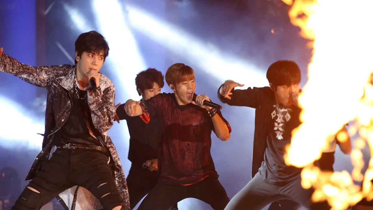 Integrantes de um grupo de K-pop cantam e dançam no palco diante de chamas cenográficas.