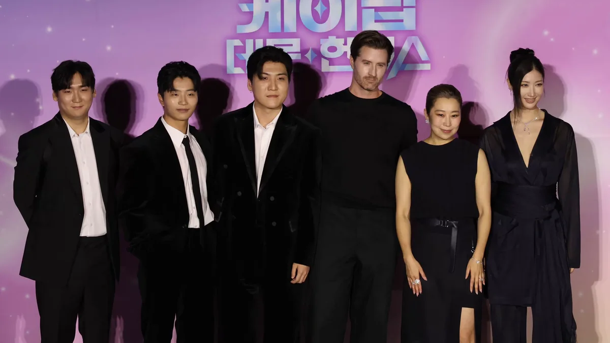 Six membres de l’équipe de KPop Demon Hunters posent devant un fond rose