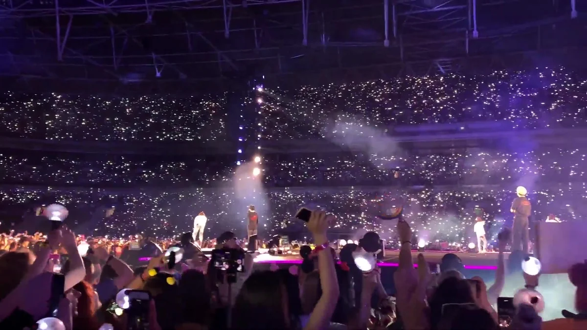 BTS members onstage seen behind fans raising light sticks and phones
