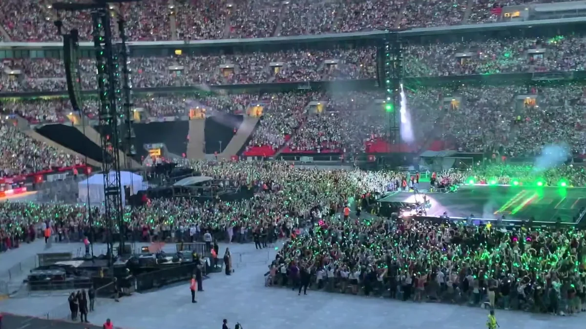 A crowd fills a stadium floor and stands beside a stage lit in green