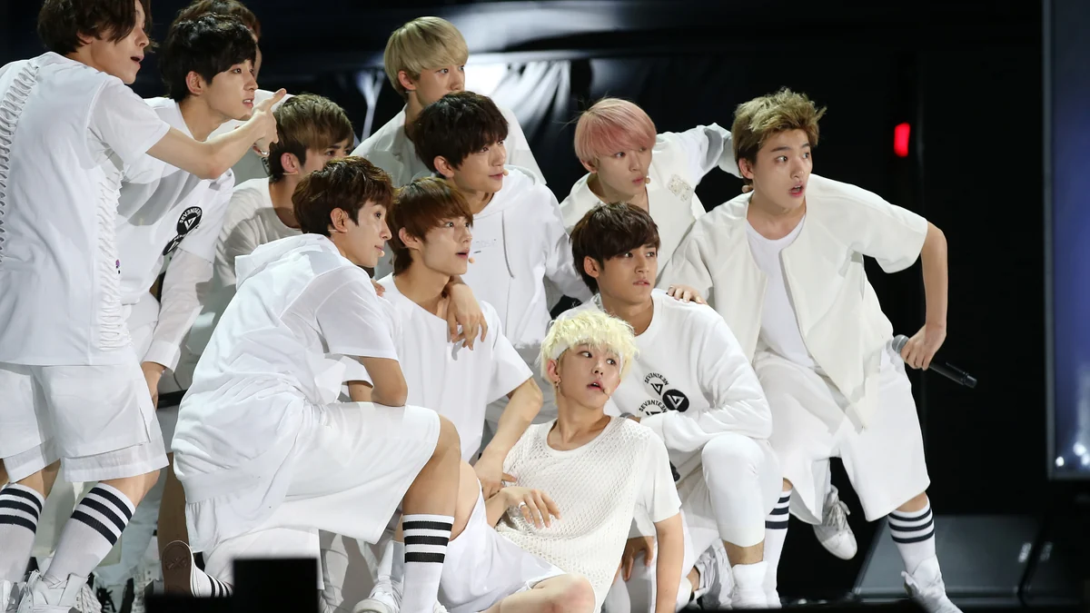 SEVENTEEN members dressed in white gather together during an onstage performance.