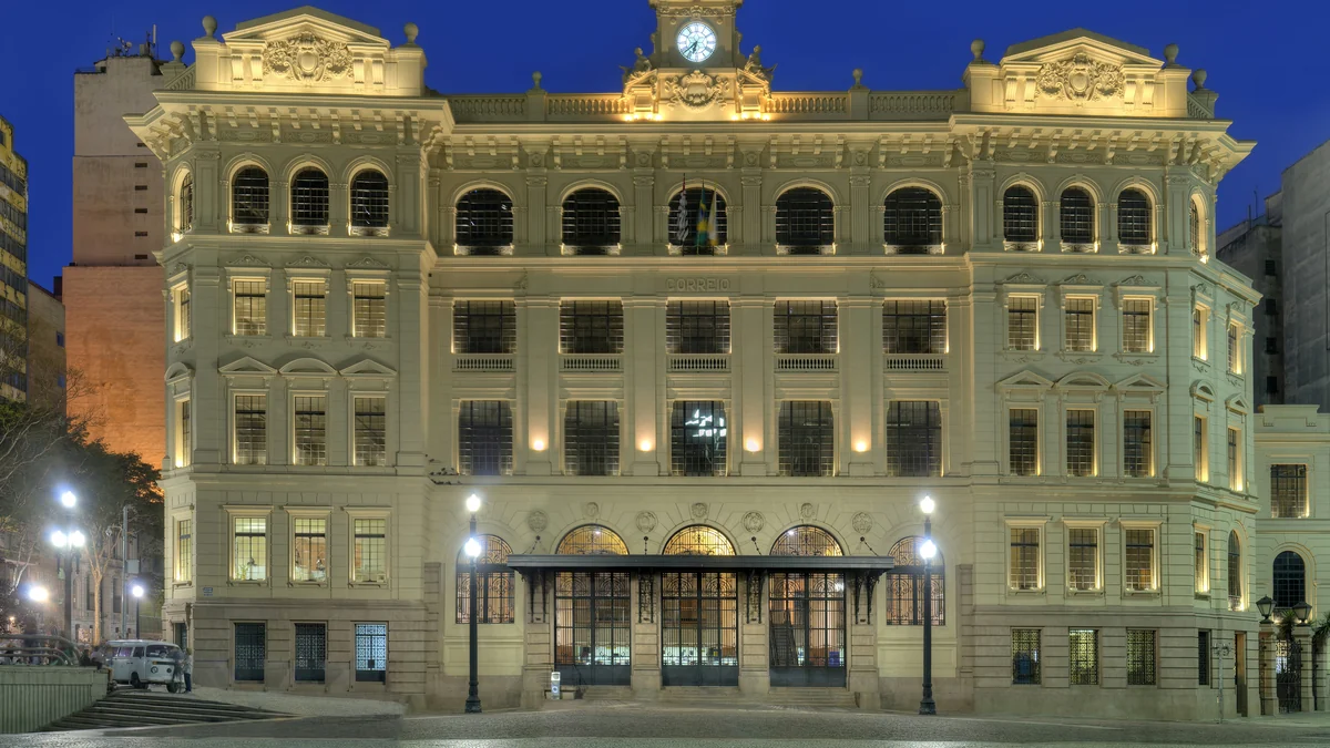 Fachada iluminada de un edificio histórico de Correios, con un reloj en la parte superior, de noche.