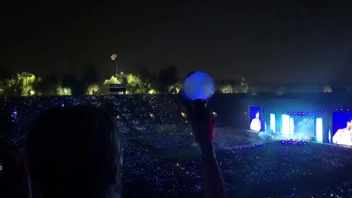 Audience with light sticks facing a blue-lit stage at a BTS concert